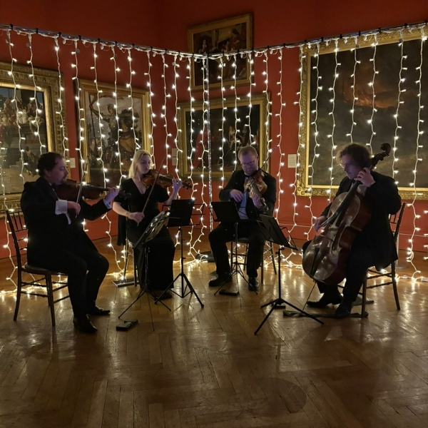 A string quartet performs in a room adorned with hanging string lights, with paintings on the walls.