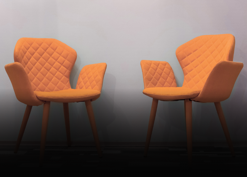 Two orange quilted chairs with wooden legs stand against a light blue wall on a striped floor.